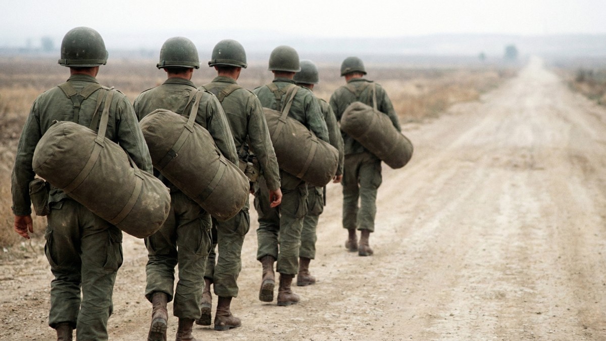 soldiers carrying cylindrical canvas military duffle bags over their shoulders