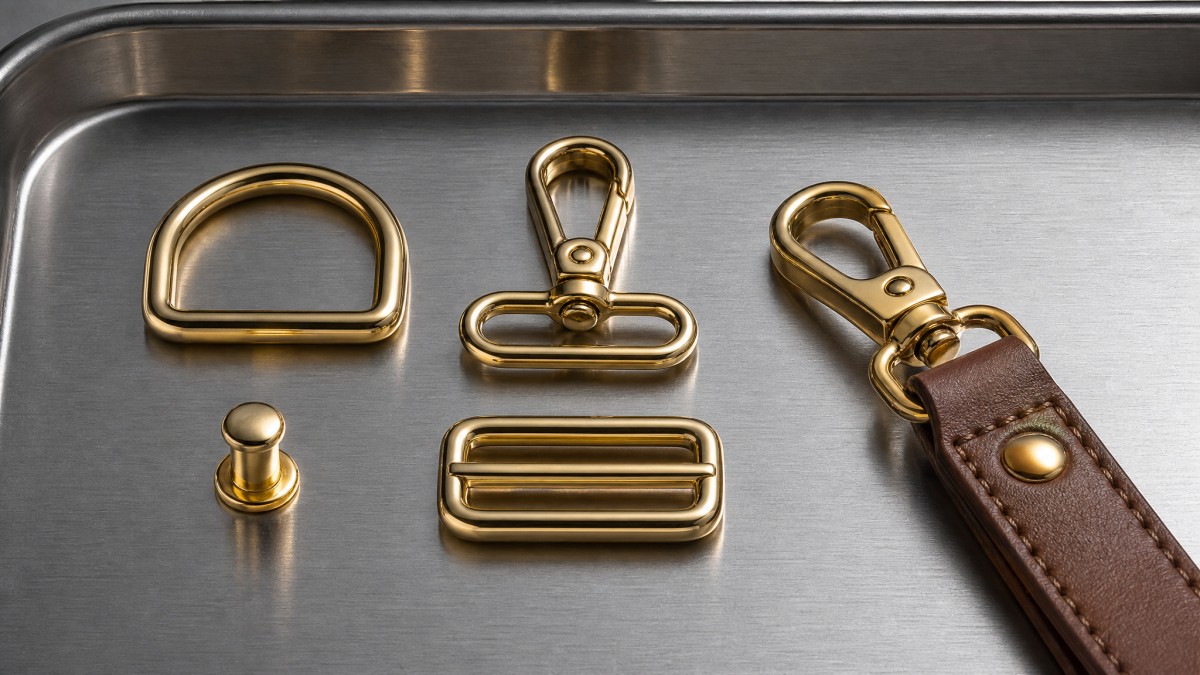 Macro shot of five bag strap hardware components in polished gold finish