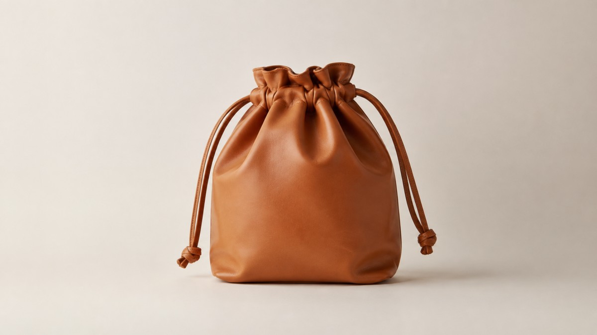 Leather drawstring bag against a plain warm off-white wall